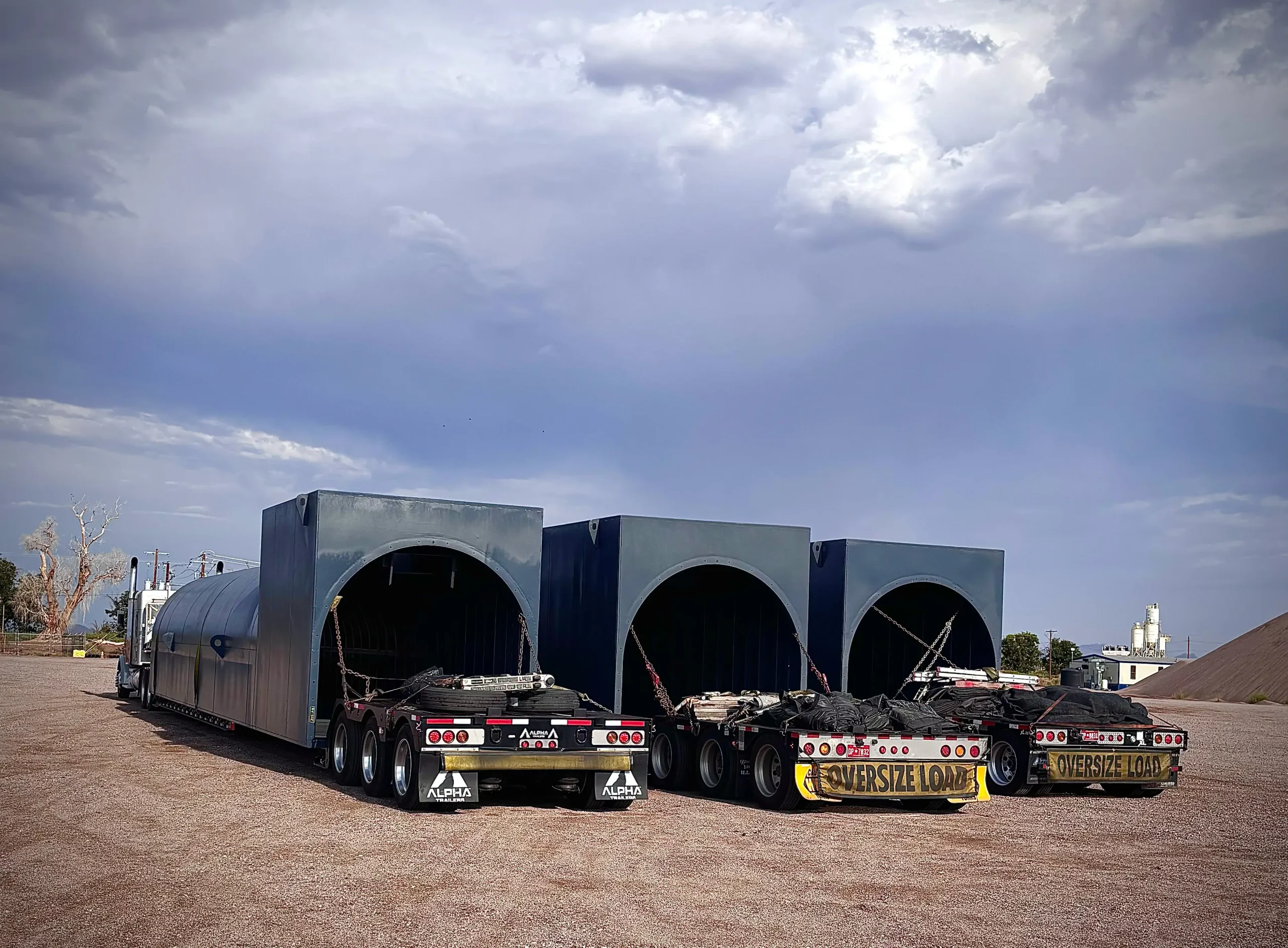 Three oversized steel culvert sections chained down on a multi-axle Tavus Transportation lowboy trailer