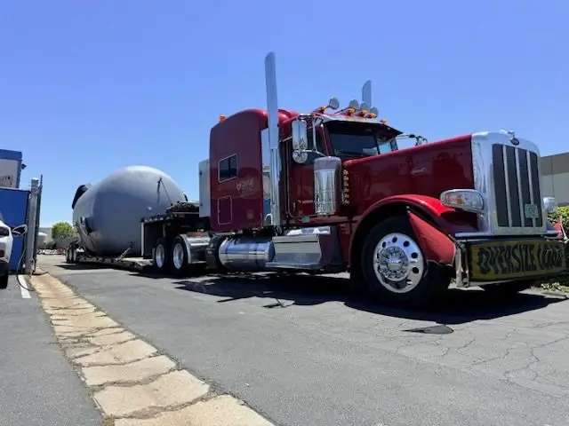 Red Peterbilt hauling a large pressure vessel under an oversize load permit